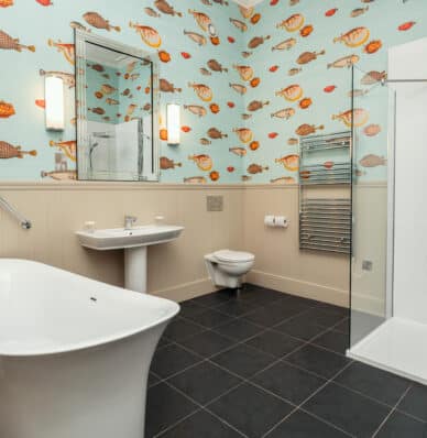 Spacious, modern bathroom with freestanding bath, fish-themed wallpaper, and glass shower; perfect for a relaxing stay.