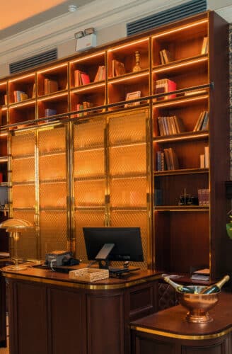 Elegant hotel reception with vintage decor, stained glass windows, ornate wallpaper, and welcoming flowers.