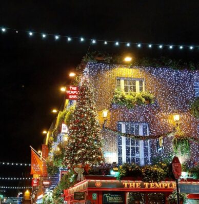 Festively lit brick hotel exterior with lush greenery, enchanting fairy lights, and a welcoming atmosphere at night.