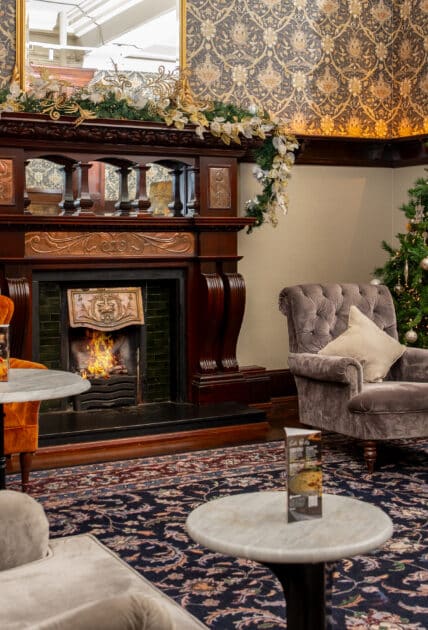 Cosy hotel lounge with elegant fireplace, plush seating, festive Christmas tree, and intricate wallpaper for a warm experience.