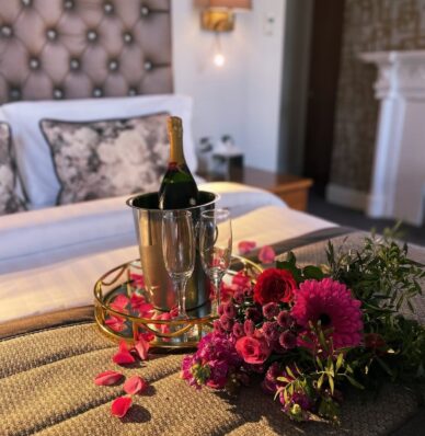 Luxurious hotel room with plush bedding, champagne, elegant décor, romantic flowers, and warm ambient lighting.