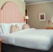 Elegant hotel room with king-size bed, plush bedding, striped headboard, desk area, and ambient lighting for a relaxing stay.