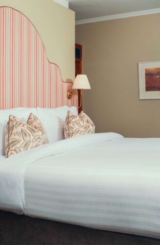 Elegant hotel room with king-size bed, plush bedding, striped headboard, desk area, and ambient lighting for a relaxing stay.