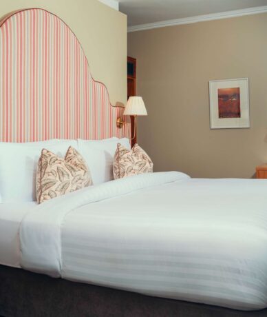 Elegant hotel room with king-size bed, plush bedding, striped headboard, desk area, and ambient lighting for a relaxing stay.