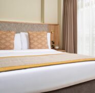 Cosy hotel room with plush double bed, stylish decor, and natural light from large windows for a relaxing stay.