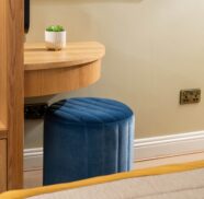 Cosy hotel room with plush blue stool, wooden desk, and modern amenities, creating a welcoming and comfortable stay.