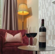 Elegant hotel room with cosy armchair, soft lighting, wine glasses and bottle; ideal for romantic getaways.