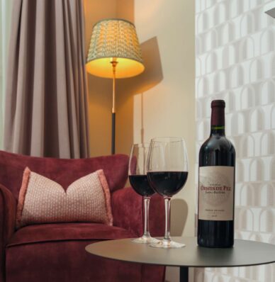 Elegant hotel room with cosy armchair, soft lighting, wine glasses and bottle; ideal for romantic getaways.
