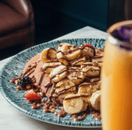 Delicious banana and chocolate pancake breakfast with fresh berries at luxury hotel restaurant, with refreshing juice.