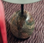 Elegant marble table on striped carpet beside plush red seating, showcasing luxurious hotel design and style.