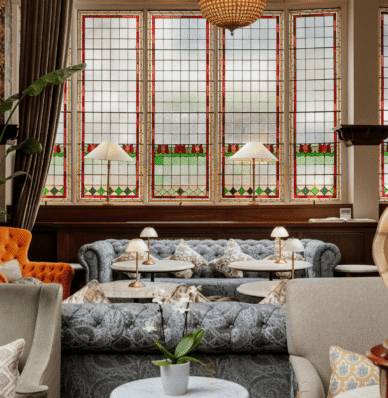 Elegant hotel lounge with plush seating, stained-glass windows, warm lighting, and coffee tables, offering a cosy atmosphere.