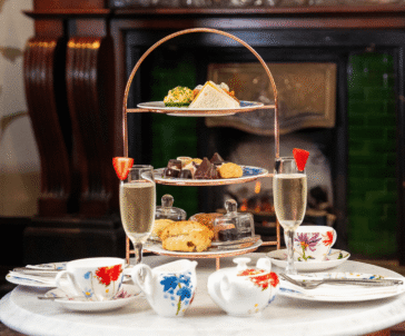 Elegant afternoon tea with pastries and champagne by a cosy fireplace at a luxury hotel.