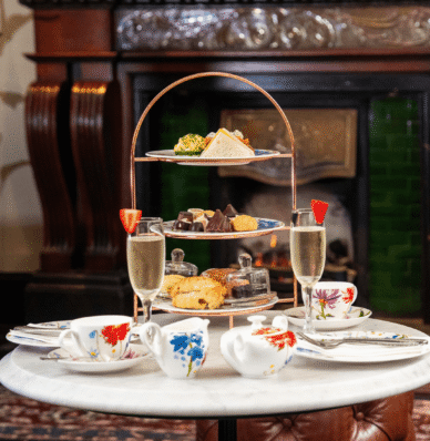 Elegant afternoon tea with pastries and champagne by a cosy fireplace at a luxury hotel.