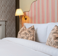 Elegant hotel room with plush bed, patterned cushions, ornate lamp, and stylish wallpaper for a relaxing stay.