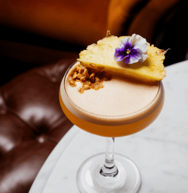 Elegant cocktail with pineapple and flower garnish on marble table at luxurious hotel lounge.