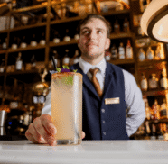 Friendly bartender serves crafted cocktail at elegant hotel bar with warm lighting and extensive drink selection.