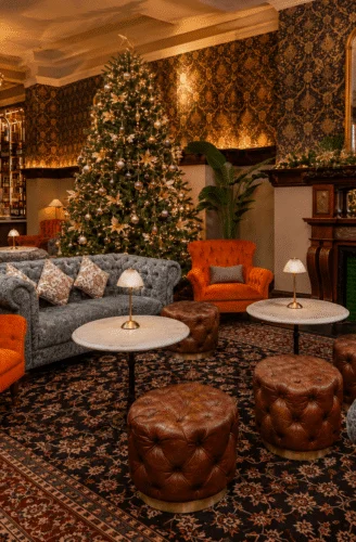 Elegant hotel lounge with Christmas tree, plush sofas, cosy fireplace, and ornate chandeliers for a warm holiday stay.