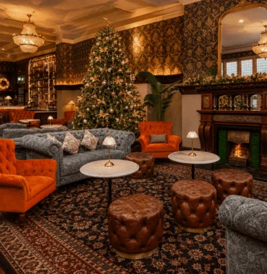 Elegant hotel lounge with Christmas tree, plush sofas, cosy fireplace, and ornate chandeliers for a warm holiday stay.